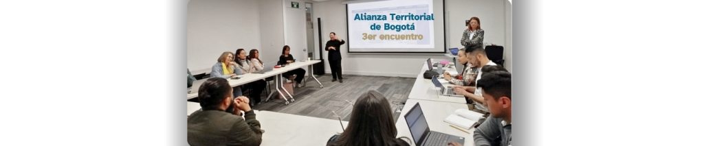 Foto de representantes de la alinaza en bgotá al rededor de una mesa cuadrada y una expositora junto al interprete de lengua de señas.